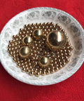 Ceramic dish with 4mm 200pcs Solid Pure Copper Balls - Brass Ball Bead showcasing various sizes on a red background.