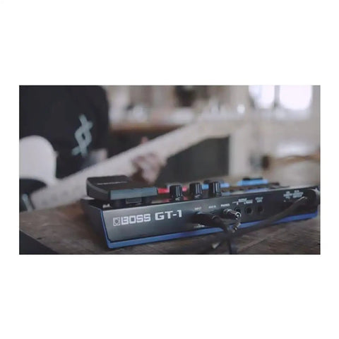 GT1 Compact Guitar Effects Processor With Amps And Effects Premium Sound Engine on table with guitarist playing in background