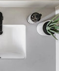 Top view of Undermount White Bathroom Sink 16 By 11 Narrow Rectangular Vanity Sink With Overflow Vitreous China Ceramic Fits 18 Inch Vanity Opening 16 By 11 Modern Durable Bath Fixture Easy Install with faucet, plant, and soap dispenser.