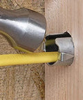 Metal nail guard for wire protection installed on a wooden stud with a yellow electrical cable, hammer nearby