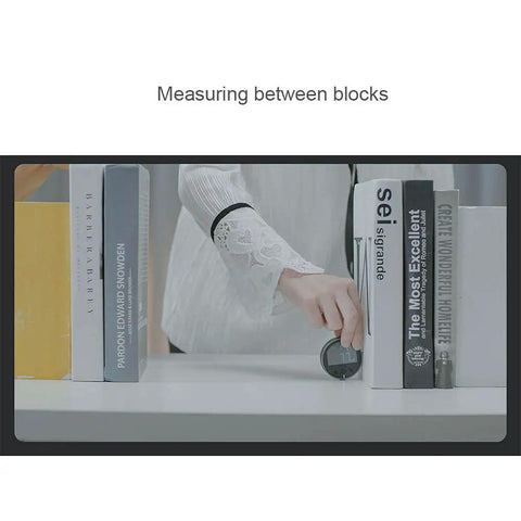 Person using Digital Tape Measure With LCD Display And Rechargeable Battery between books on a shelf.