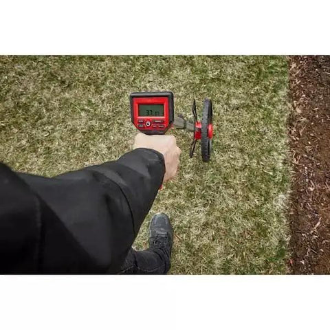 Badass Digital Measuring Wheel Featuring A 12 Inch Durable Metal Roller And Crisp IP54 Backlit Display measuring distance on grass.