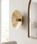 NautiGlow Modern Brass Brushed Wall Sconce with Round Backplate, Exposed Globe Light Fixture on wall near mirror.