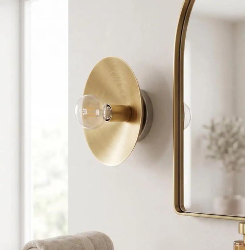 NautiGlow Modern Brass Brushed Wall Sconce with Round Backplate, Exposed Globe Light Fixture on wall near mirror.