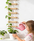 Child watering plants next to 6-Feet Extra Tall Wooden Ladder Plant Trellis For Indoor And Outdoor Use, 15-Section Natural Wood Climbing Support For Vines Ivy Pothos Monstera, Sturdy Rust-Free Easy Assembly Dope Space-Saving For Balconies And Gardens.