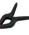Close-up of a black nylon spring clamp with cushioned grip, part of Six Pack 9 Inch Hefty Spring Clamps Made From Tough Nylon With Cushioned Jaw Tips Engineered For Knockout Grip Efficiency And Quick Swaps On Woodworking Or Photo Studio Crafting Sessions.