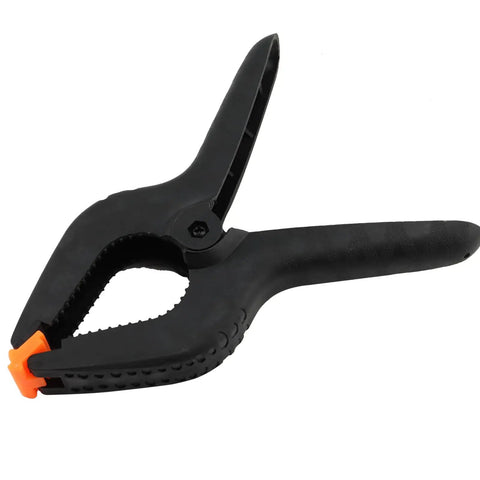 Close-up of a black nylon spring clamp with cushioned grip, part of Six Pack 9 Inch Hefty Spring Clamps Made From Tough Nylon With Cushioned Jaw Tips Engineered For Knockout Grip Efficiency And Quick Swaps On Woodworking Or Photo Studio Crafting Sessions.