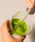 Person using Matcha Starter Kit With Electric Whisk And Milk Frother For Home Barista Vibes to mix bright green matcha in a glass
