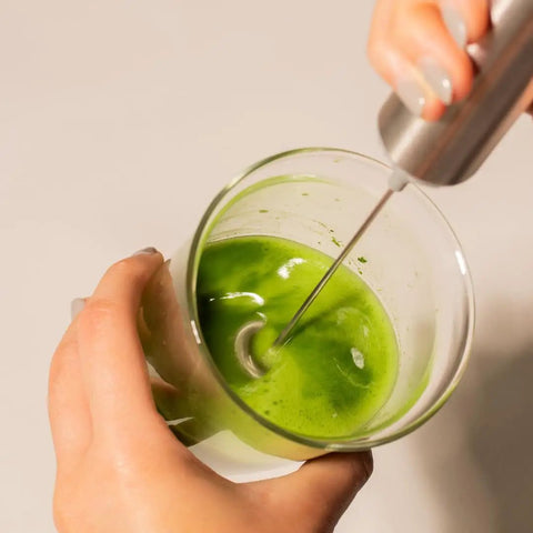 Person using Matcha Starter Kit With Electric Whisk And Milk Frother For Home Barista Vibes to mix bright green matcha in a glass