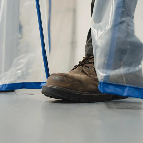 E-Z UP magnetic dust containment door kit, outdoors, close-up of brown boot entering a clear plastic door with blue trim.