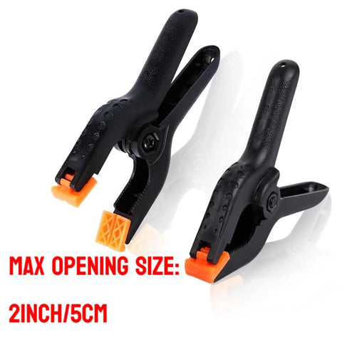 Two black plastic large spring clamps with orange tips, angled view.