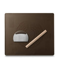 Brown silicone baking mat with an angled metal dough scraper and wooden rolling pin placed on top.