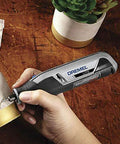 Dremel Lite cordless rotary tool side view, gray with blue logo, used on a brass metal cylinder.