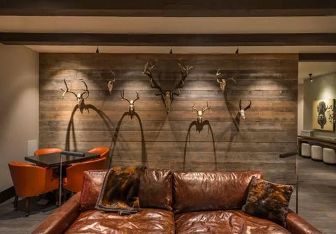 Interior of a rustic living room featuring a leather sofa, wooden wall with antlers, and a dining table.