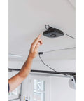 Hand reaching toward MyQ-Garage Wi-Fi hub installed on garage ceiling – Control Your Garage Door From Your Phone Anywhere Open It On The Go Monitor It And Get Real Time Alerts With The MyQ-Garage System Works With Most Openers Made After 1993.
