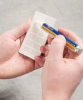 Fluke Networks NFC-SOLVENTPEN fiber optic cleaning solvent pen, blue body with yellow label, held in hands.