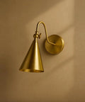 Lupe Wall Sconce Brass with Perforated Shade and Bowtie Swivel mounted on wall, showcasing industrial chic design.