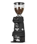 Calibrated Automatic Espresso Tamper Always Nailing The Perfect Shot With Adjustable Pressure Settings Fits Fiorenzato F64 58mm Portafilter Black Smooth Operator Game Changer side view with coffee beans in hopper.