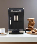 Fully Automatic Espresso Machine With Stainless Steel Cup Warmer And Smart Sensors For Low Water Beans Or Full Grounds Container Customizes Your Go To Drinks, in classic black with coffee cup and snacks.