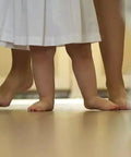 Bare feet of a child and adult visible, standing on a heated floor indoors, illustrating comfort provided by Element Non Programmable Floor Heating Thermostat With Dual Voltage 120 240V, No Fuss Floor Temperature Sensor, Built In GFCI For Radiant Floor Heating Cable Systems.