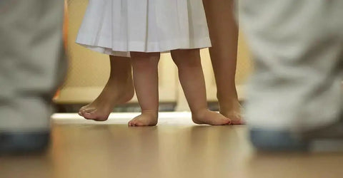 Bare feet of a child and adult visible, standing on a heated floor indoors, illustrating comfort provided by Element Non Programmable Floor Heating Thermostat With Dual Voltage 120 240V, No Fuss Floor Temperature Sensor, Built In GFCI For Radiant Floor Heating Cable Systems.