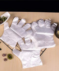 Disposable transparent plastic food-prep gloves laid flat on a metal rack on a wooden table