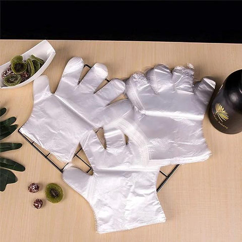 Disposable transparent plastic food-prep gloves laid flat on a metal rack on a wooden table