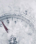 Snow-covered outdoor thermometer showing temperatures below zero.