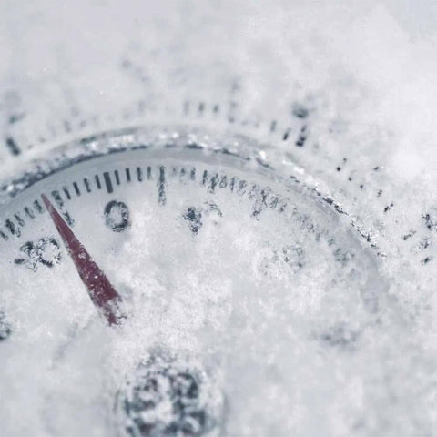 Snow-covered outdoor thermometer showing temperatures below zero.