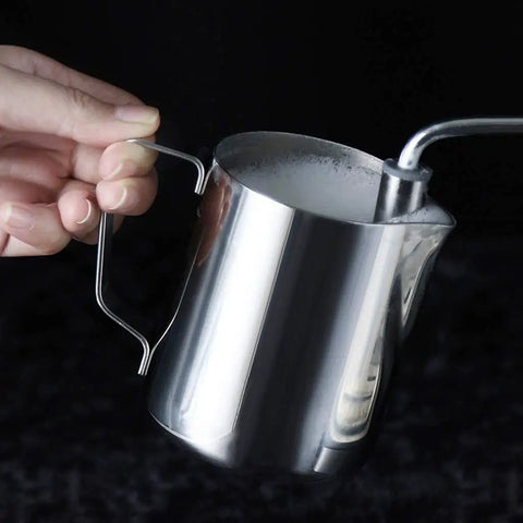 Stainless steel milk frothing pitcher held in hand, ideal for creating lattes, cappuccinos, and espresso drinks.