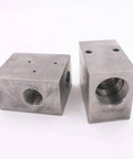 Two metal square pneumatic valve body blocks with threaded holes.