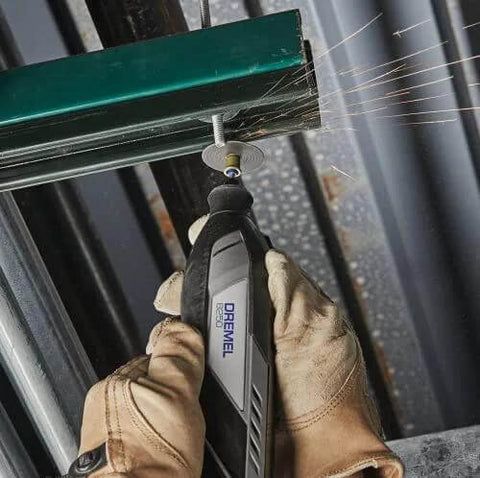 Dremel cordless rotary tool close-up; gray body with Dremel logo, sparks from metal grinding.