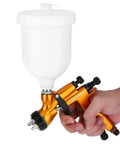 Heavy-Duty 1.3mm Gravity Paint Sprayer With High Atomization Pneumatic Airbrush held in hand, featuring a large white cup for paint.