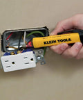 Hand using non-contact voltage tester on open socket, part of Electrical Test Kit With IR Digital Thermometer Multimeter Non Contact Voltage Tester Pen And Receptacle Tester 4 Piece Set For Pros And DIYers Ideal For Home Projects And Pro Grade Electrical Diagnostics On The Job.
