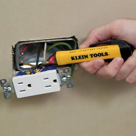 Hand using non-contact voltage tester on open socket, part of Electrical Test Kit With IR Digital Thermometer Multimeter Non Contact Voltage Tester Pen And Receptacle Tester 4 Piece Set For Pros And DIYers Ideal For Home Projects And Pro Grade Electrical Diagnostics On The Job.