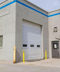 Heavy Duty Beefy Steel Safety Barrier Bollard And Industrial Traffic Control Post With Rock Solid Bright Yellow Finish And Concrete Fillable Base Plate For Warehouse Machine Guard At 42 Inches near a warehouse loading dock.