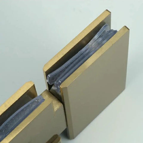 Close-up of Rock Solid Frameless Glass Shower Door Hinge For Modern Bathrooms in brushed gold finish with glass panels.