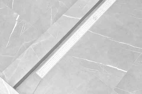 Rock Solid 304 Stainless Steel Linear Shower Drain Kit With Matte White Grid and Broad Hair Catcher installed on tiled surface.