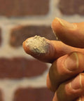 Close-up of Mor-Flexx Gray Acrylic Latex Caulk for mortar, stucco, and grout repair on fingertip, showing textured application.