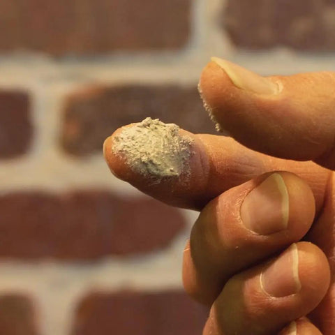 Close-up of Mor-Flexx Gray Acrylic Latex Caulk for mortar, stucco, and grout repair on fingertip, showing textured application.
