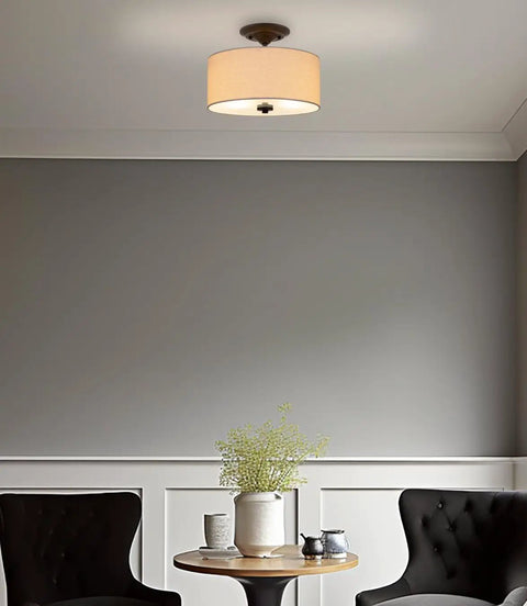 Addison 13 Inch Dope Modern Drum Semi Flush Mount Ceiling Light With Off White Fabric Drum Shade Two Light Fixture In Oil Rubbed Bronze Finish For Kitchen Hallway Living Space, installed in a cozy room setting with chairs.