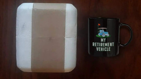 Sweet Retirement Ride Golf Cart Coffee Mug In 15 Oz Black Ceramic next to packaged item on wooden surface.