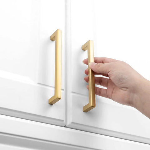Hand reaching for Top Shelf 10 Pack Brushed Gold Cabinet Pulls 5 Inch Square Bar Drawer Handles on white cabinets.