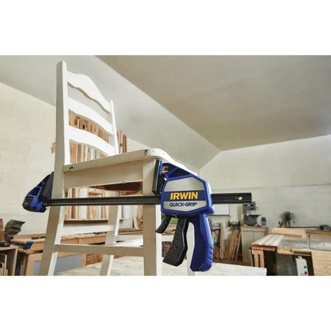 Heavy Duty One Handed Bar Clamp With Quick Change Spreader Removable Swivel Jaws holding a white chair in a workshop.