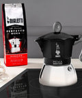 Heavy Duty Moka Induction Coffee Maker With Rock Solid Stainless Steel Boiler And Premium Aluminum Lid Brews Smooth Two Cup Espresso That Nails Your Morning Kickstart In Deep Black on a countertop with coffee.