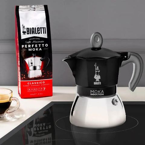 Heavy Duty Moka Induction Coffee Maker With Rock Solid Stainless Steel Boiler And Premium Aluminum Lid Brews Smooth Two Cup Espresso That Nails Your Morning Kickstart In Deep Black on a countertop with coffee.