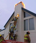 Firefighters using a ladder to extinguish flames from a chimney, showcasing urgent rescue action during a flue fire.
