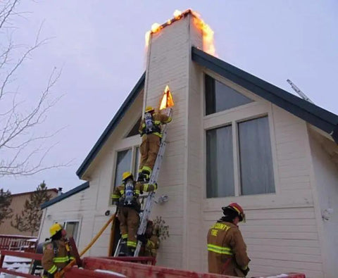 Firefighters using a ladder to extinguish flames from a chimney, showcasing urgent rescue action during a flue fire.