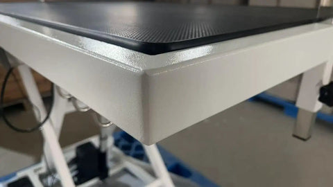 Close-up of the edge of Heavy Duty Electric Dog Grooming Table With Smooth Operator Foot Pedal And Kickass Sturdy X Frame For Easy Height Adjustments And No Sweat Pet Styling In White.