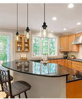 Three Pack Black Industrial Pendant Lights With Clear Glass Shades above a kitchen island with dark countertop and wooden cabinets.